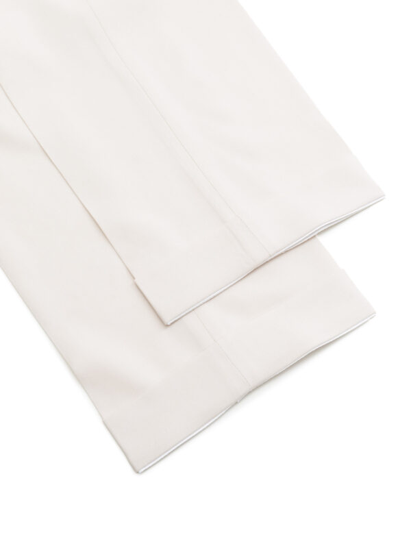 Zbliżenie na mankiety nogawek jasnych spodni garniturowych z widocznym starannym wykończeniem podwinięcia.