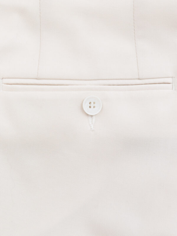 Tylny detal kieszeni spodni garniturowych w kremowym, zapinanej na jasny guzik