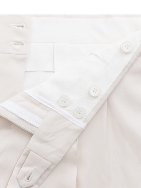 Wnętrze pasa spodni garniturowych w jasnym kolorze, z widocznym białym guzikiem i zapinką.