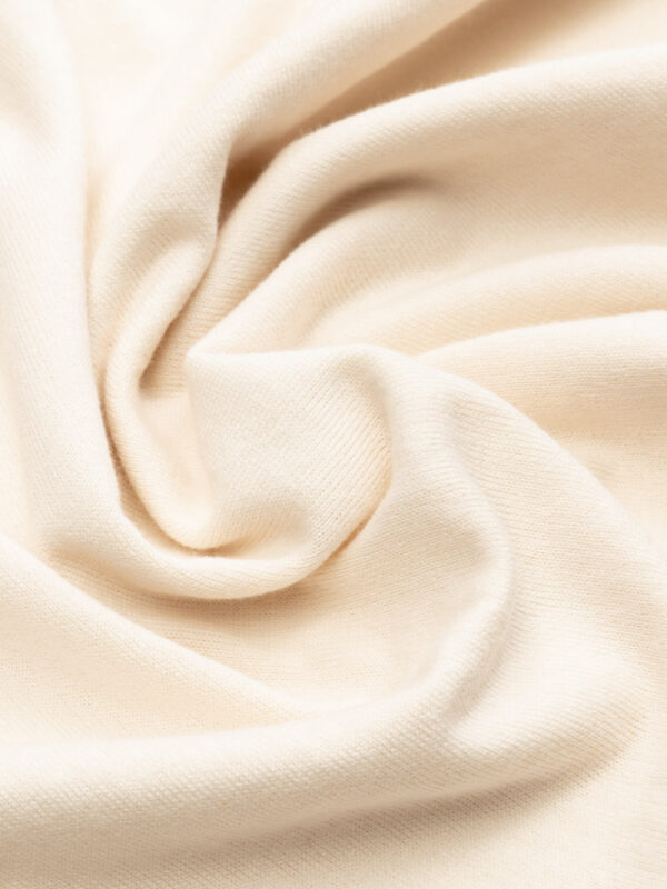 Materiał jasnobeżowego T-shirtu złożony w artystyczne fałdy.