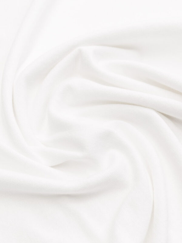 Materiał białej koszulki polo ułożony w luźne fałdy, pokazujący fakturę dzianiny.